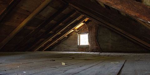 Empty unfinished attic with bare rafters, plank floor and a small gable window