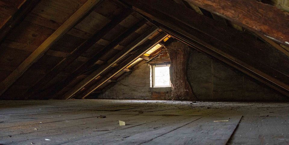 Empty unfinished attic with bare rafters, plank floor and a small gable window