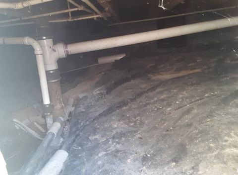 Crawl space under a house with drain pipes and a vapor barrier over the dirt