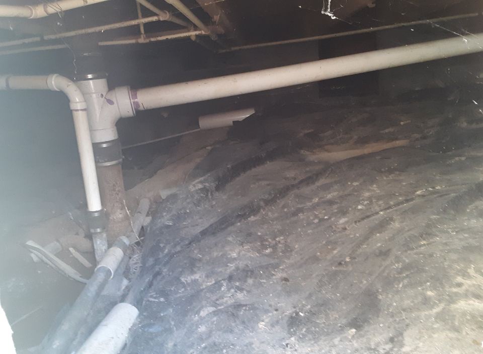 Crawl space under a house with drain pipes and a vapor barrier over the dirt